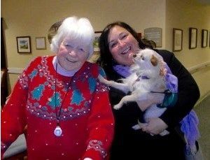 Two women are holding a small white dog in their arms.