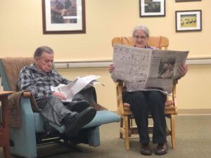 A man and a woman are sitting in chairs reading newspapers