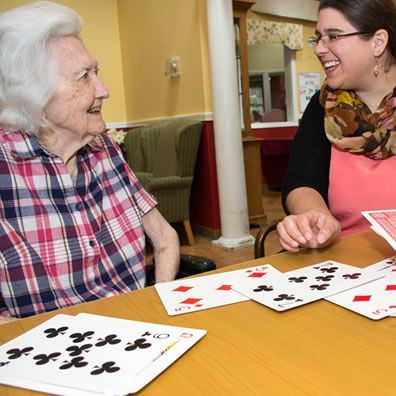 Two women are sitting at a table with playing cards and smiling