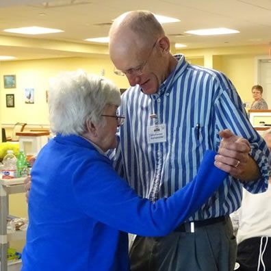 A man in a striped shirt is dancing with a woman in a blue jacket