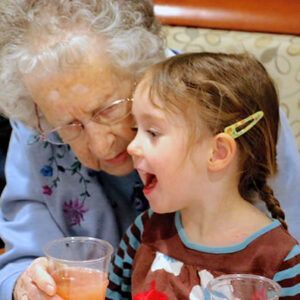 An elderly woman is holding a glass of orange juice next to a little girl.