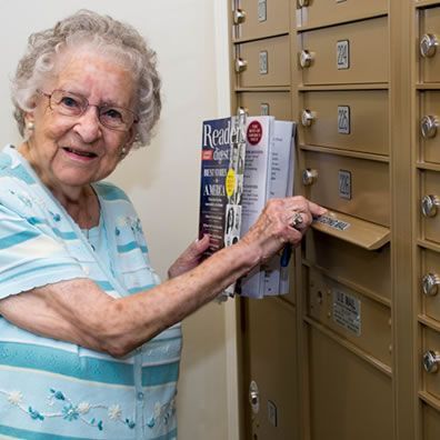 An elderly woman is putting a book into a mailbox.