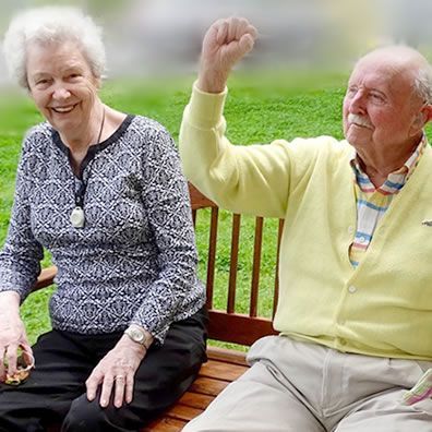A man and a woman are sitting on a bench with their arms in the air.