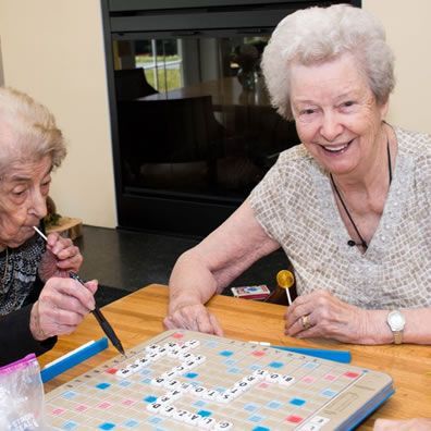 Two elderly women are sitting at a table playing scrabble