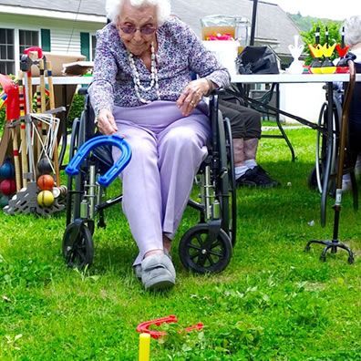 An elderly woman in a wheelchair is playing a game in the grass.