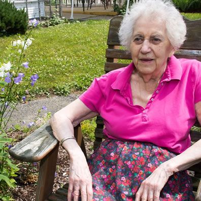 An elderly woman is sitting on a wooden bench in a park.
