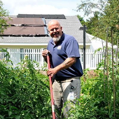 A man is standing in a garden holding a shovel.