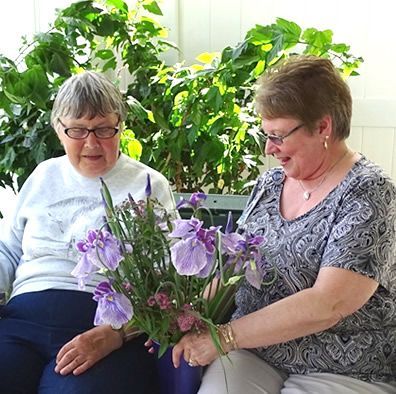 Two women are sitting on a couch holding purple flowers