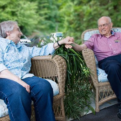A man and a woman are sitting in wicker chairs talking to each other.