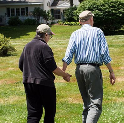 Two men are walking in a grassy field holding hands