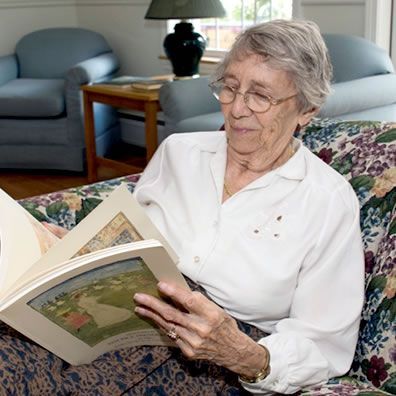 An elderly woman is sitting on a couch reading a book