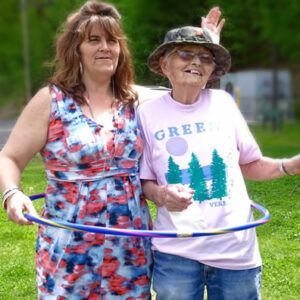 Two women are standing next to each other in a park holding hula hoops.