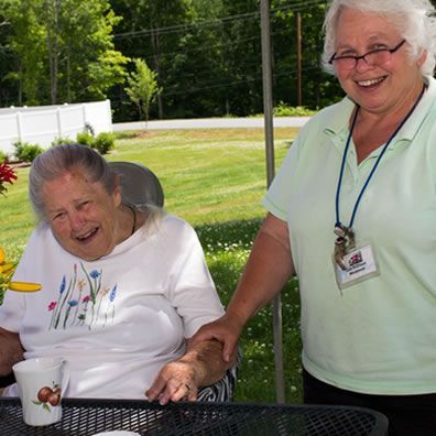 A woman in a green shirt is standing next to an older woman in a wheelchair.