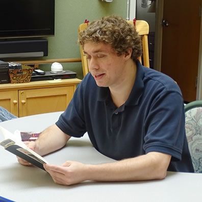 A man in a blue shirt is sitting at a table reading a book