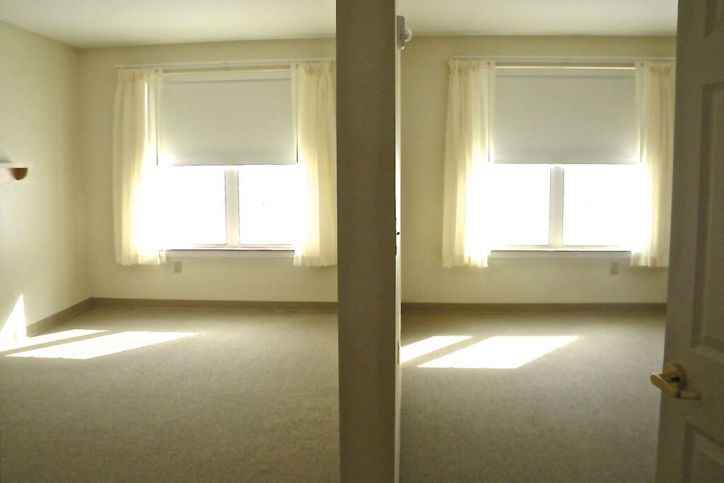 An empty room with two windows and white curtains