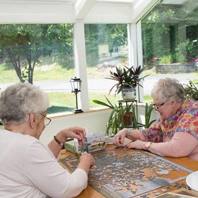 Two older women are sitting at a table playing a puzzle.