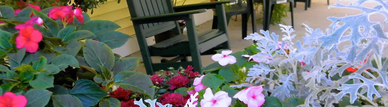 A rocking chair is sitting on a porch surrounded by flowers.