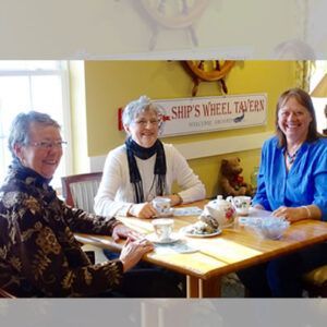 Three people are sitting at a table in front of a sign that says ship 's wheel tavern