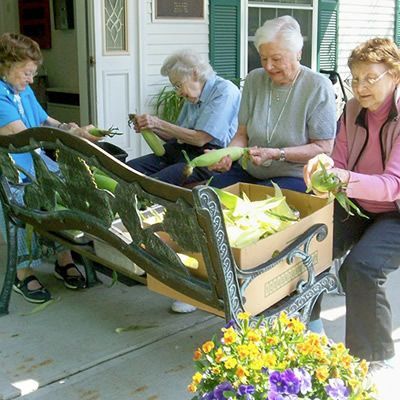 A group of women are sitting on a bench holding corn on the cob