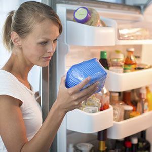 A woman is holding a blue container in front of a refrigerator.