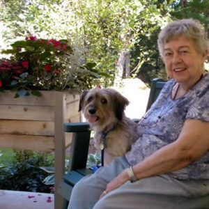 An elderly woman is sitting on a bench with her dog