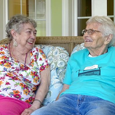 Two older women are sitting on a couch talking to each other.