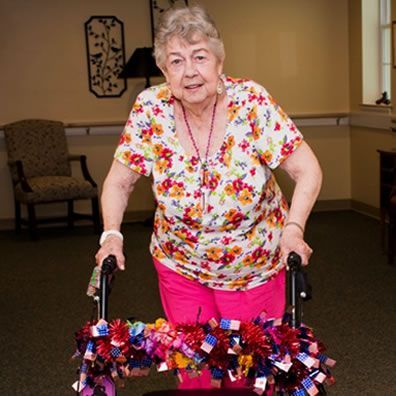 An elderly woman is using a walker decorated with pom poms