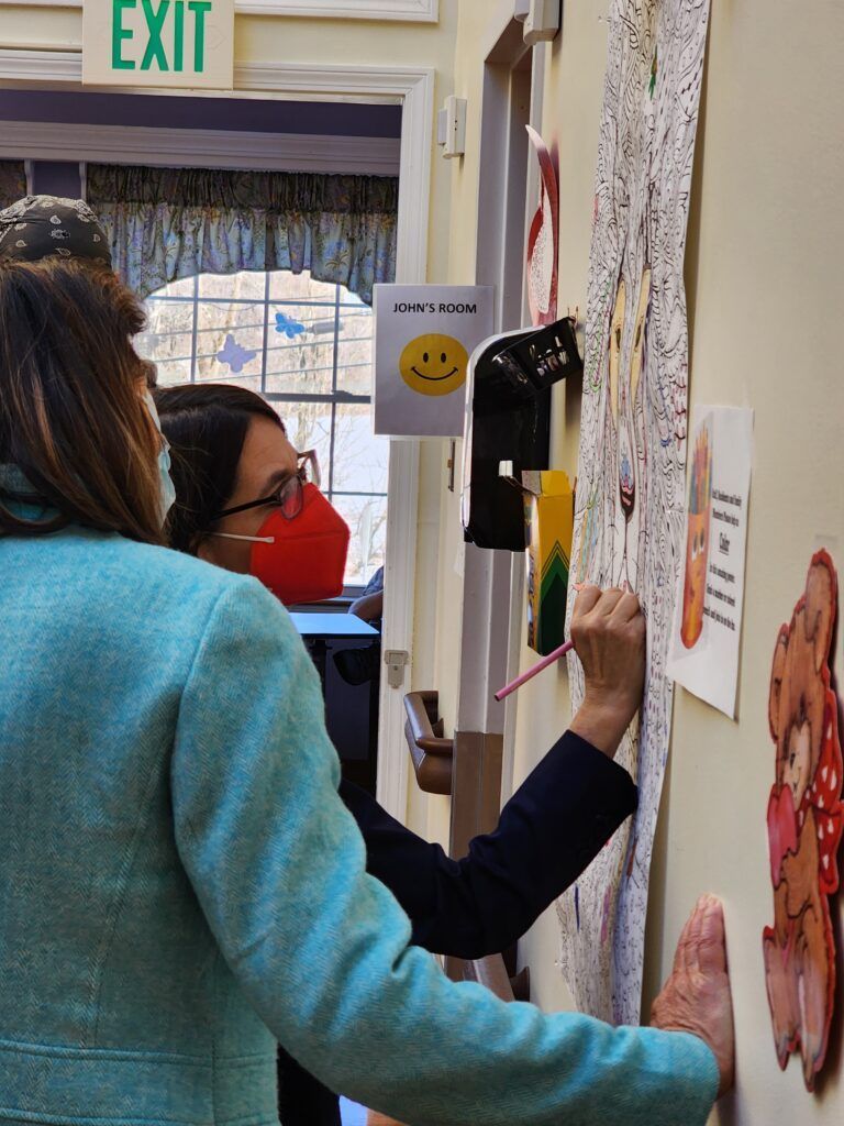 A woman wearing a mask is writing on a wall in front of an exit sign