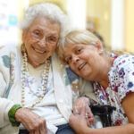 An elderly woman is sitting next to a younger woman in a wheelchair.