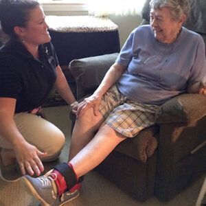 A woman is kneeling down next to an older woman sitting in a chair.