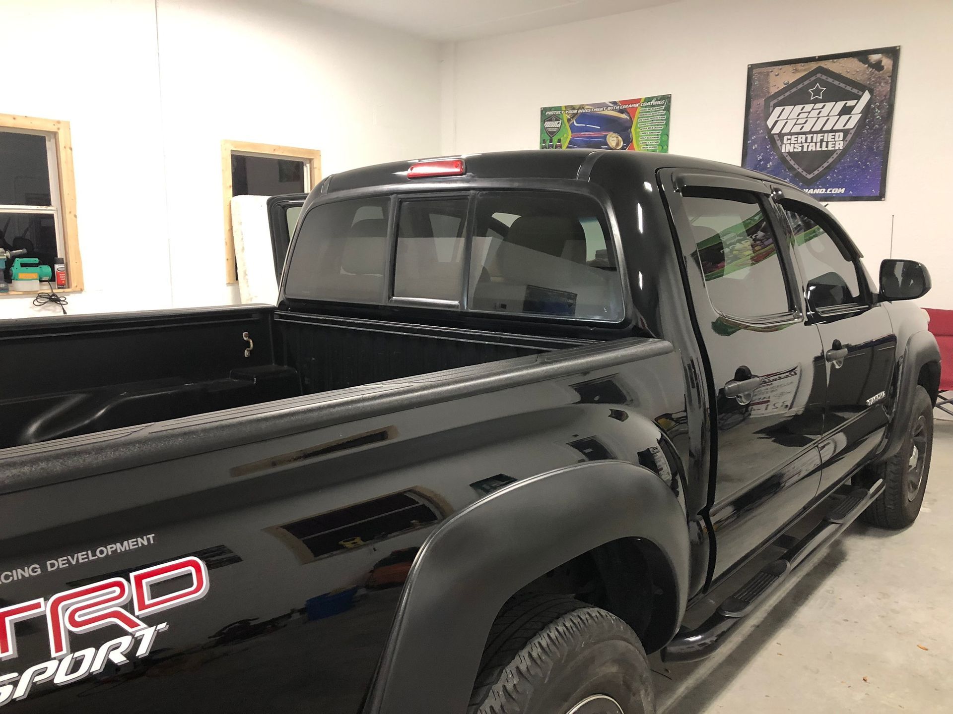Black Toyota Tacoma truck in a garage with TRD Sport emblem, tinted windows, and black fender flares.