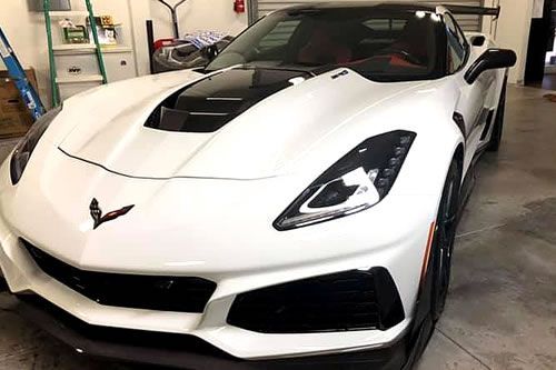 White Corvette sports car with black accents, parked indoors.