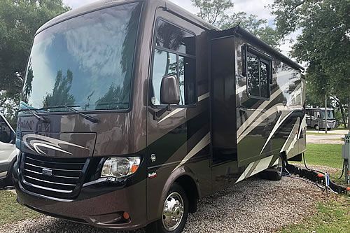 Brown and tan RV parked outdoors with its awning extended.