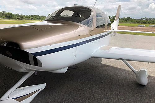 Gold and white single-engine aircraft parked on a tarmac.