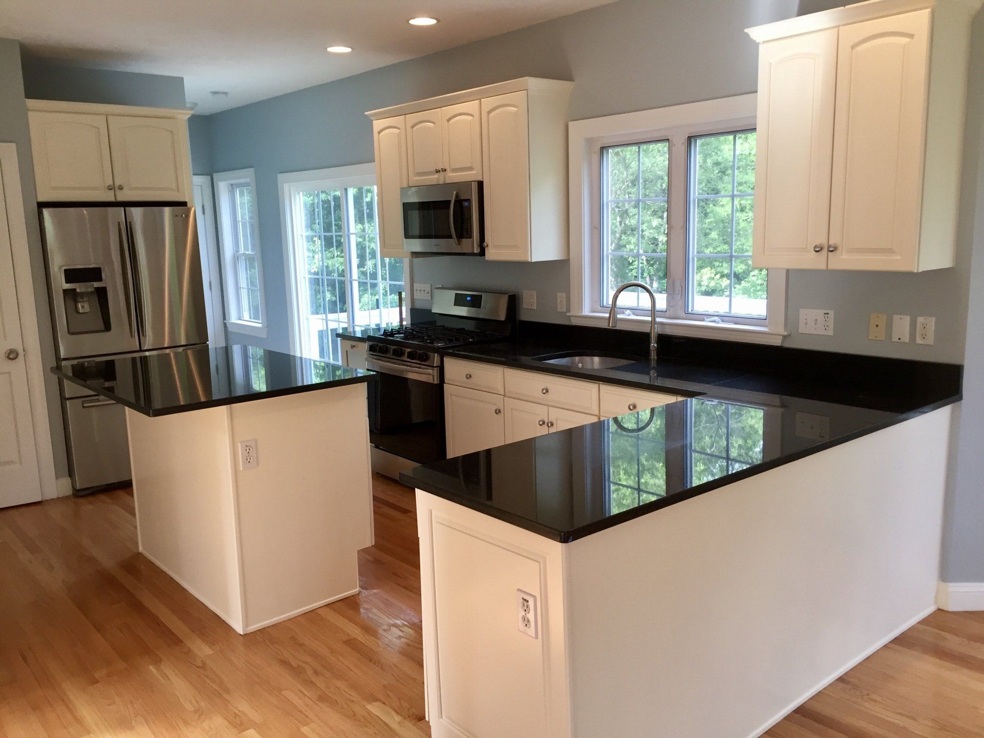 A kitchen with white cabinets , black counter tops , stainless steel appliances , and hardwood floors.