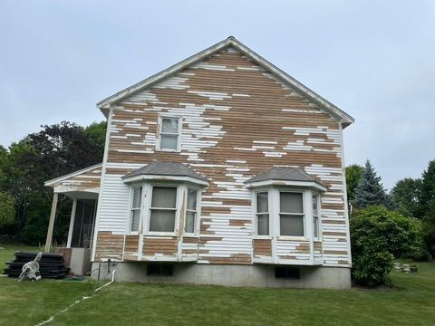 A white house with brown siding is sitting on top of a lush green field.