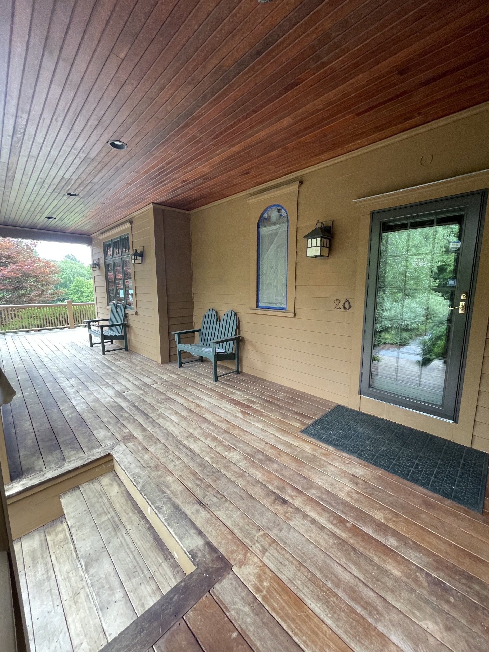 A large wooden porch with a bench and chairs on it with faded porch boards