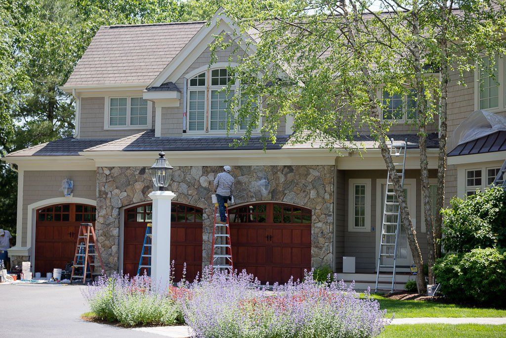 A man on a ladder is painting the side of a house.
