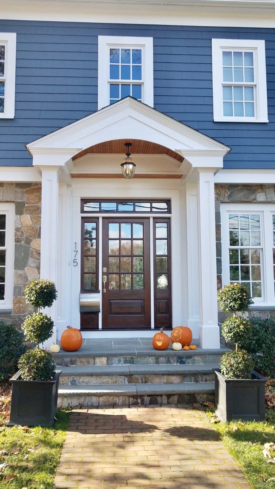 The front door of a blue house with pumpkins on the porch.