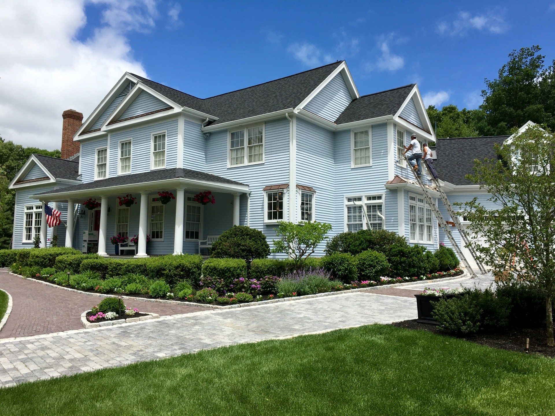 A man is painting the side of a large blue house.