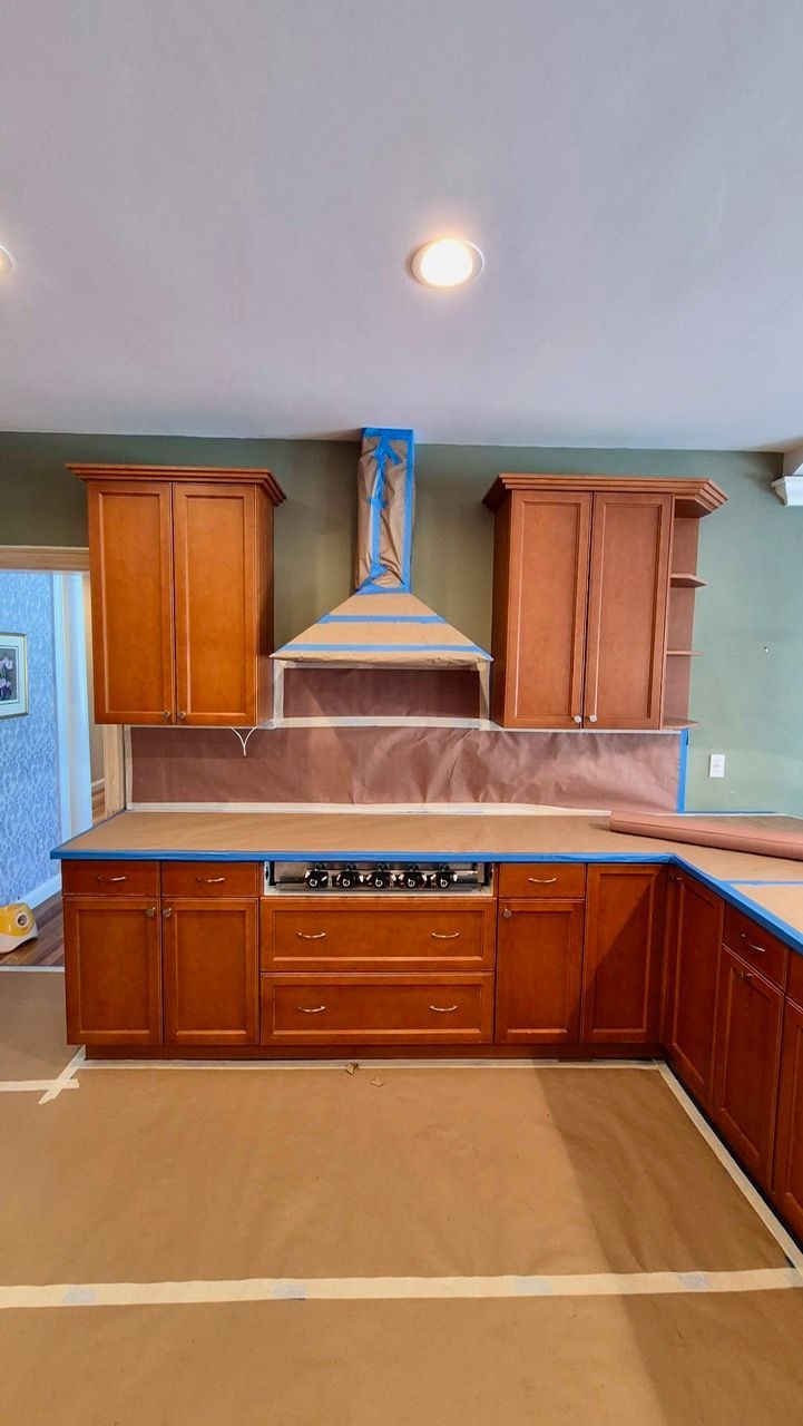Before cabinet painting showing honey wood cabinets masked with blue painter's tape and countertops protected during Laperle Painting kitchen transformation in Medfield