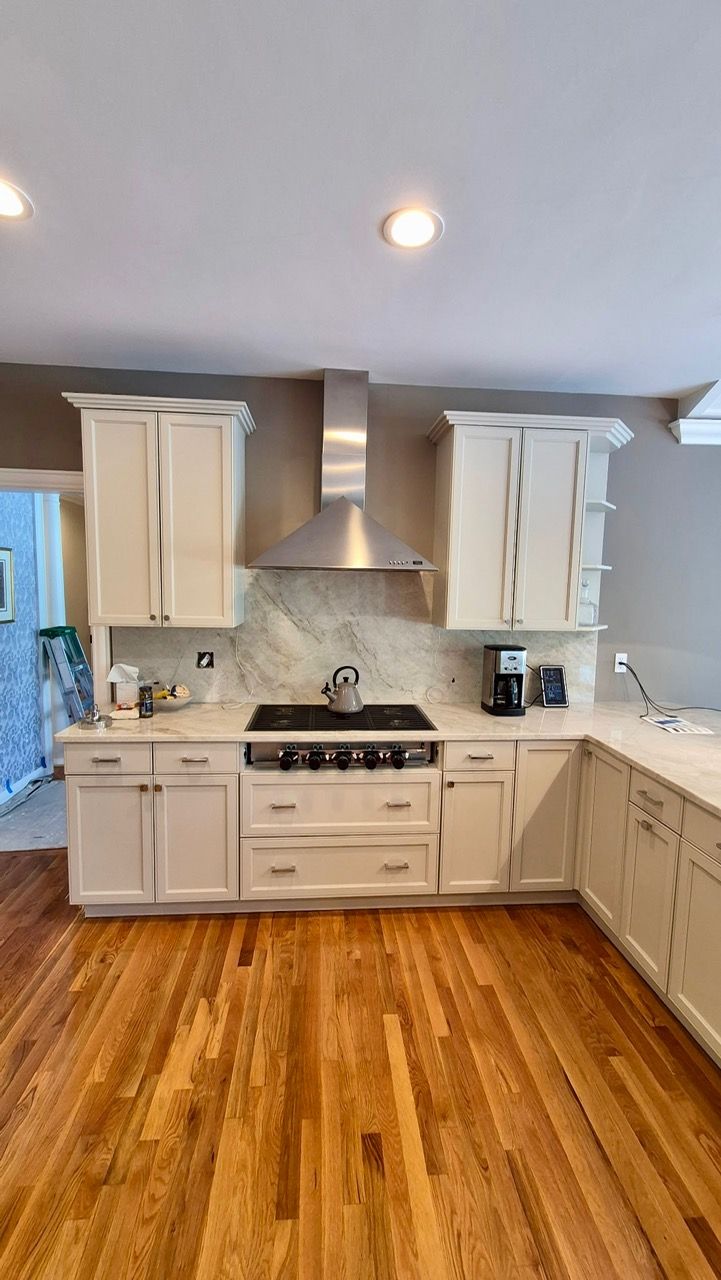 White painted kitchen cabinets with marble backsplash and stainless steel range after professional cabinet painting in Medfield MA