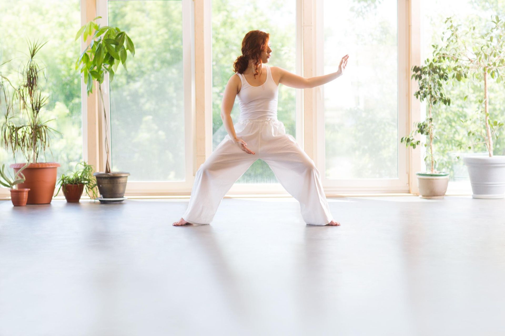 A woman is practicing tai chi in a room with potted plants.