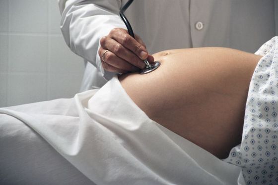 Un médico examina el vientre de una mujer embarazada con un estetoscopio.