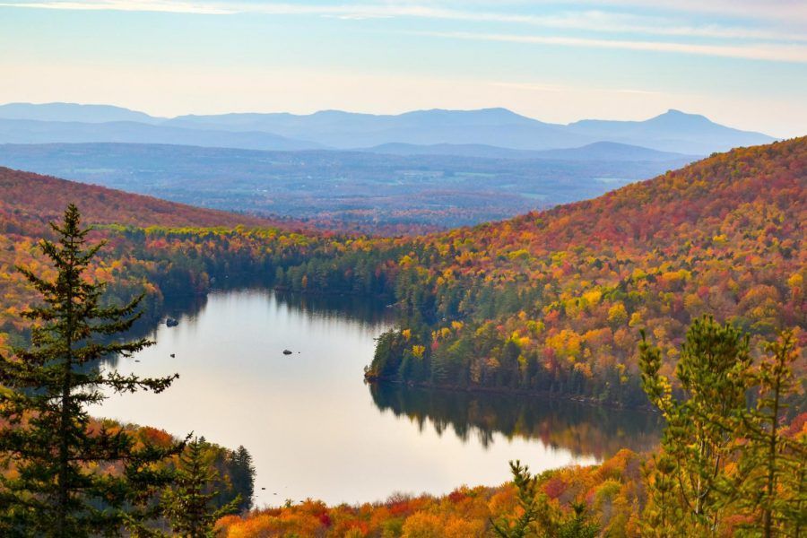 Autumnal lake surrounded by vibrant orange and yellow trees, under a blue sky with clouds.