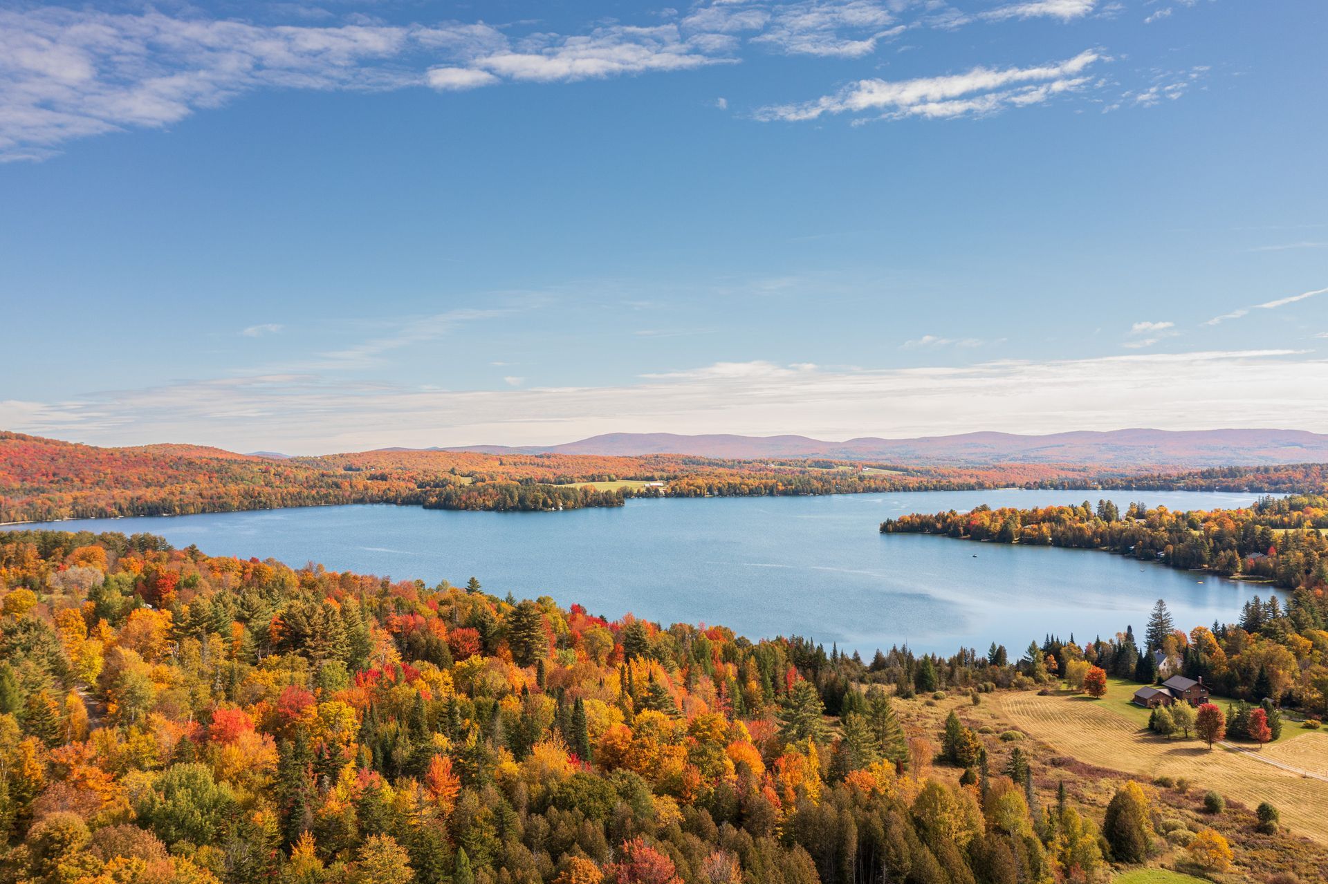 Autumn landscape with lake surrounded by vibrant fall foliage under a blue sky.