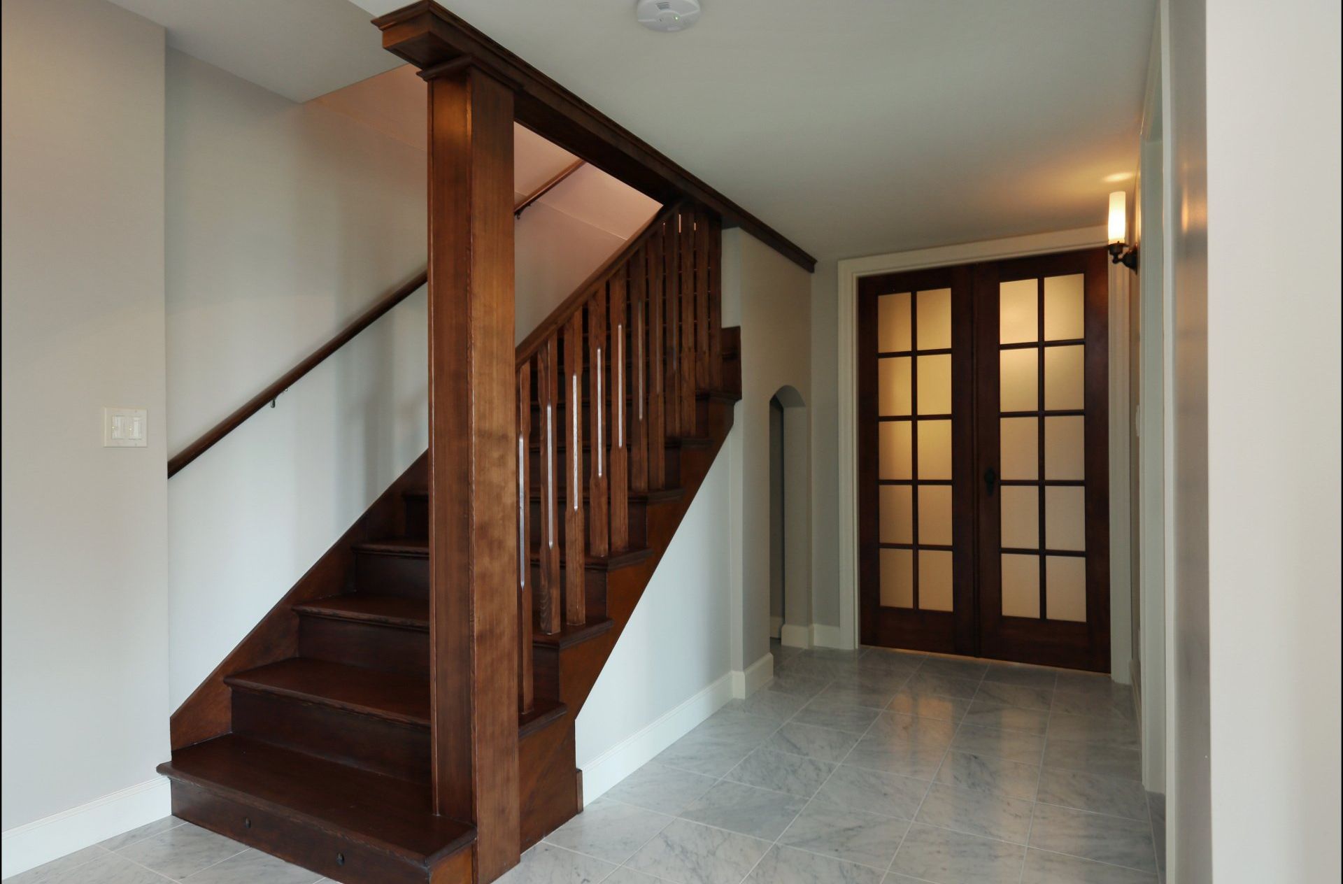An empty hallway with a wooden staircase and french doors
