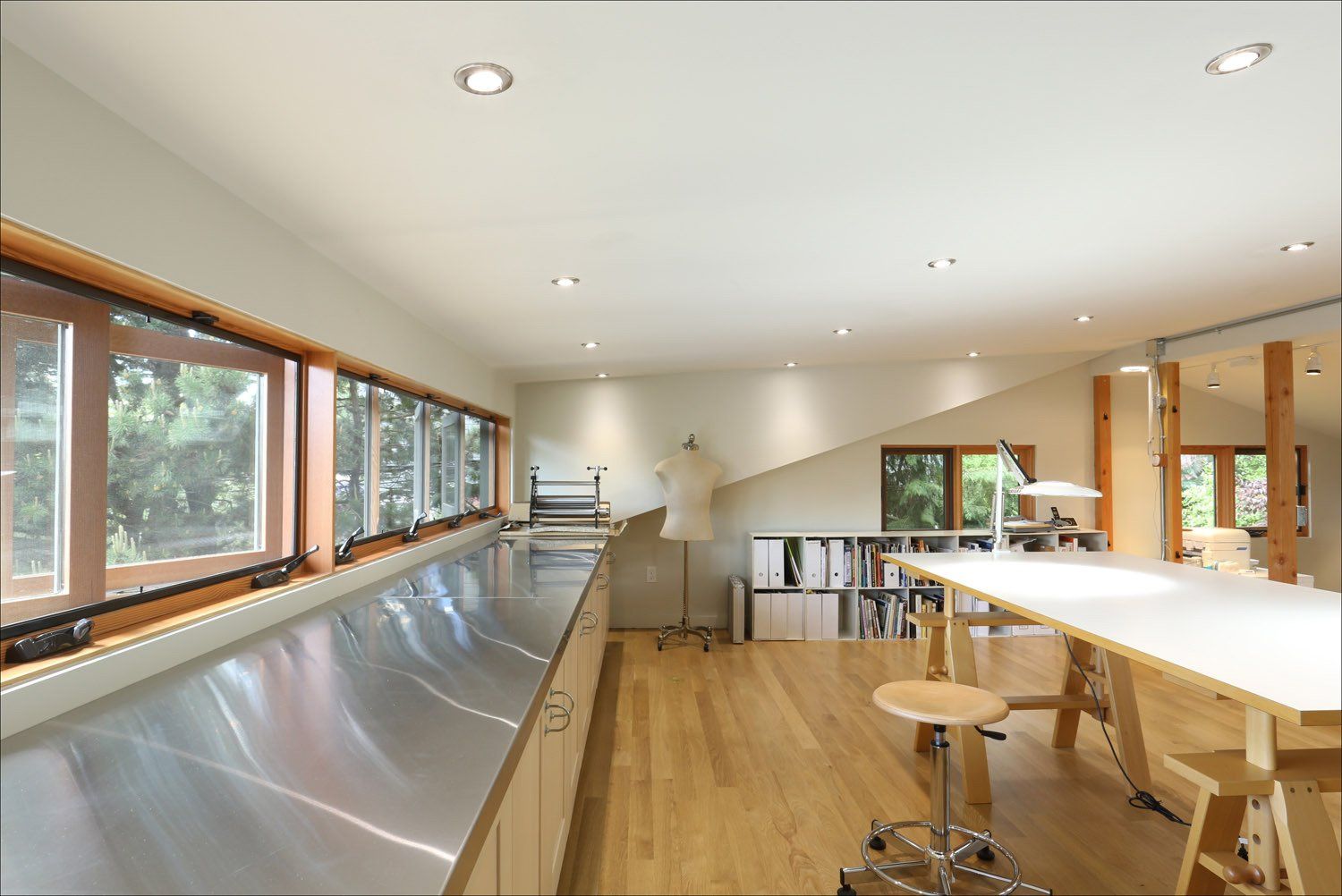 Inside the art studio with the window bank and a work surface below on the left and a large quilting table on the right.