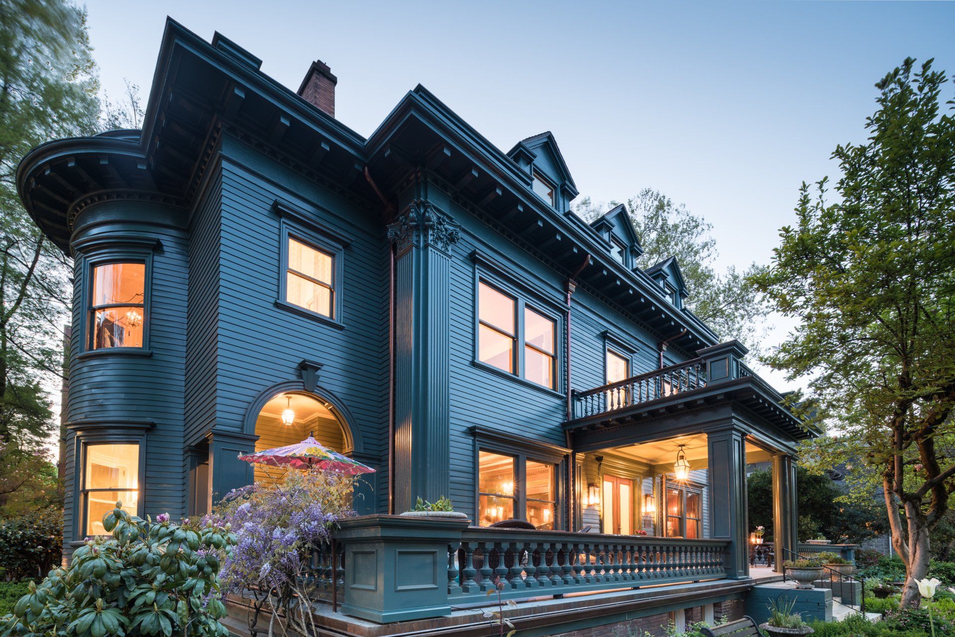Large dark-teal Colonial mansion lit during twilight hours in the spring.