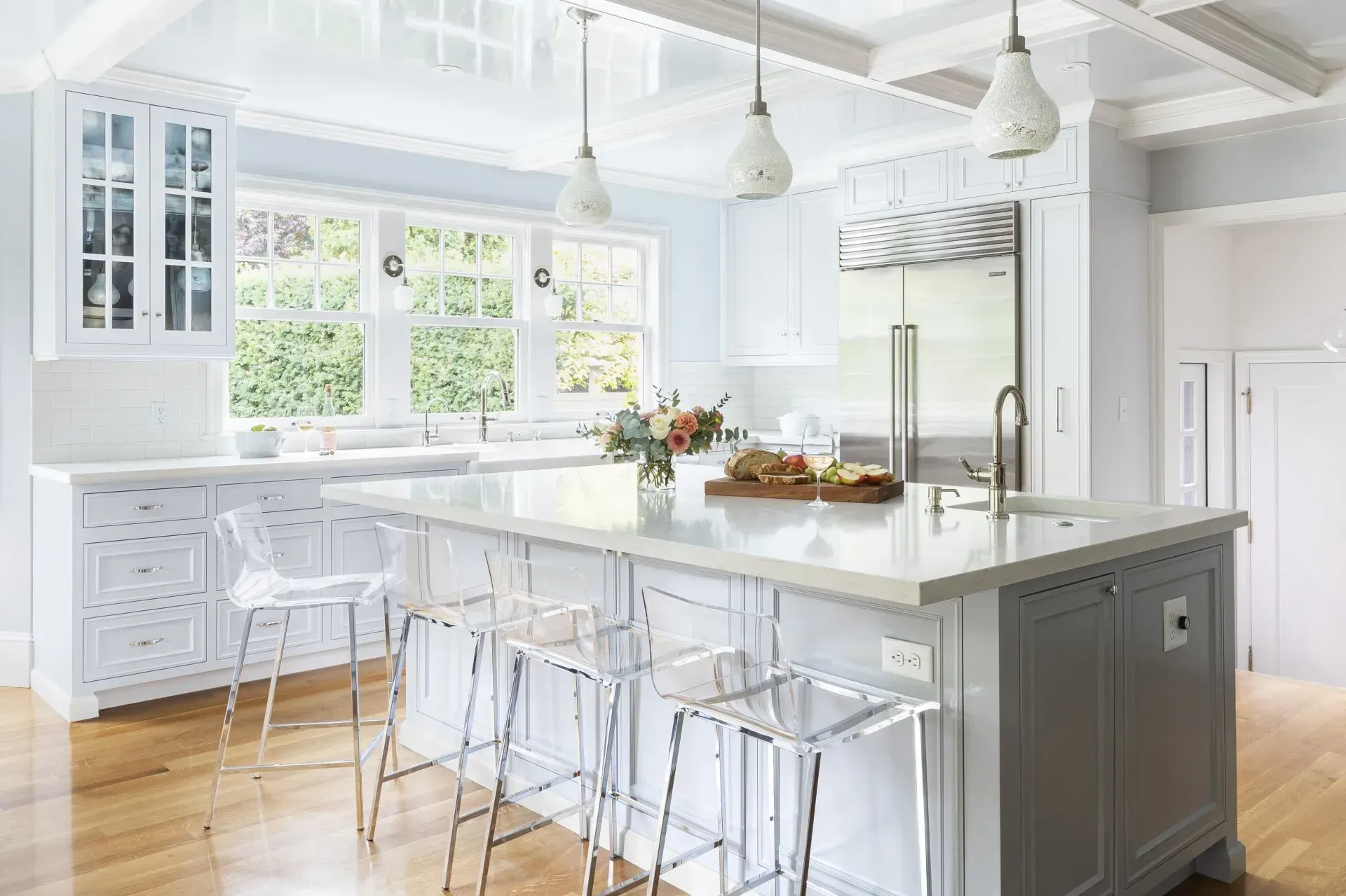 A kitchen with white cabinets , a large island , and clear stools.